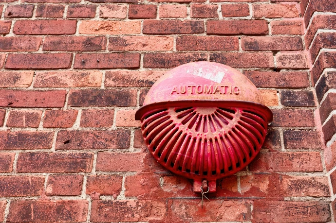 Red automatic alarm mounted on brick wall